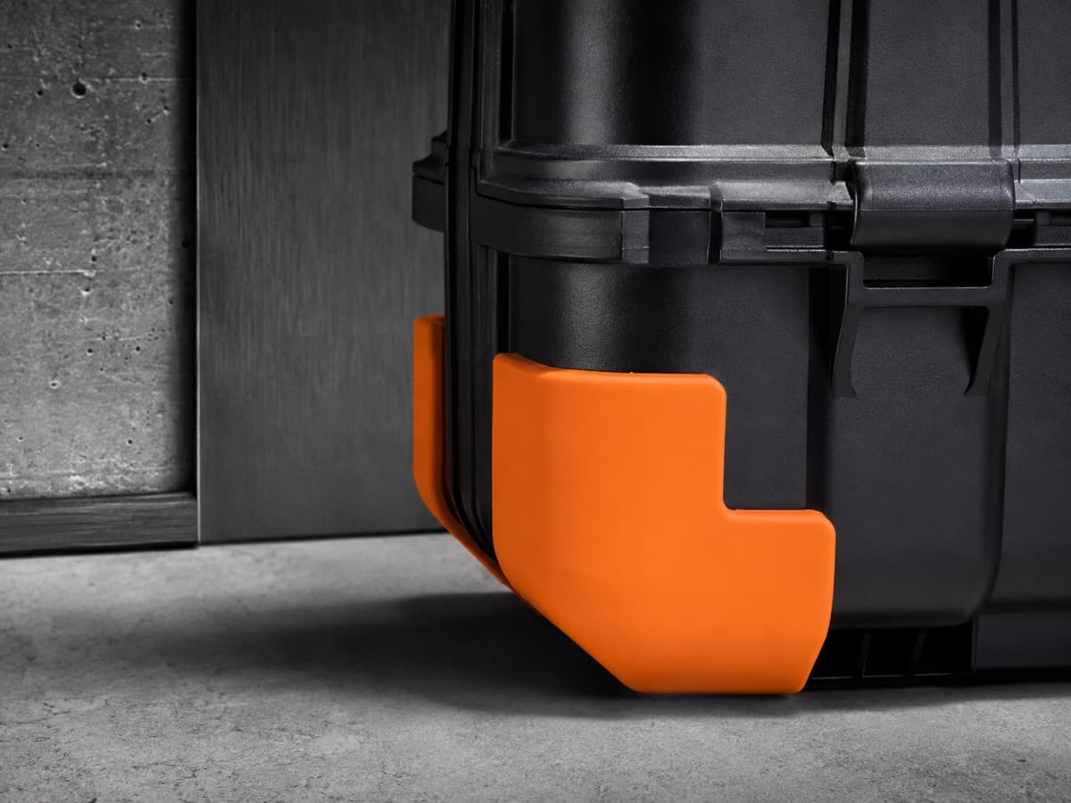 A moulded corner guard fitted to the bottom corner of a hard-shell case, its lip wrapping both faces.
