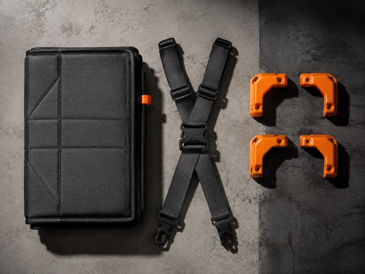 A flat-lay kit on concrete: a folded padded cover, crossing straps with a buckle, four corner guards.