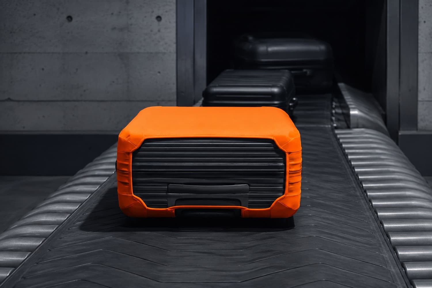 A case in a high-visibility cover riding an airport baggage conveyor belt.