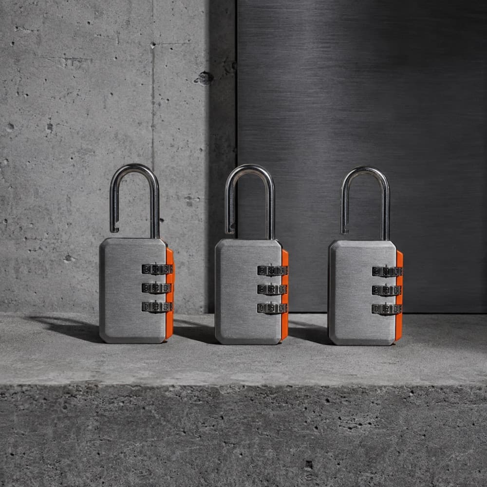 Three identical combination padlocks in a tight row on concrete, shackles open.